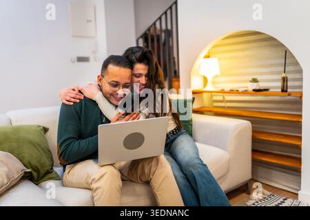 Happy couple laughing watching content on laptop Stock Photo