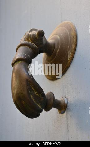 Side view of an antique brass hand-shaped door knocker on a painted grey door Stock Photo