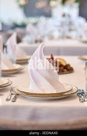 Close-up of a white decorative napkin folded on a ceramic plate. Elegant table setting for wedding banquet or fine dining event in a luxury restaurant Stock Photo