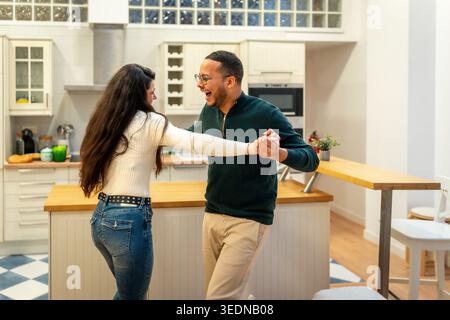 Happy diverse couple dancing and laughing in home kitchen Stock Photo