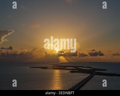 Aerial view of a long bridge stretching across the ocean towards a golden sunset with sunbeams breaking through clouds Florida, United States. Stock Photo