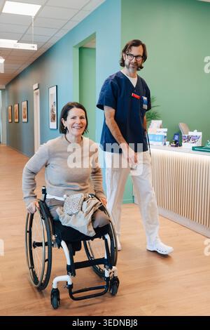 Portrait of smiling amputee woman wheeling on wheelchair near male nurse in hospital lobby Stock Photo