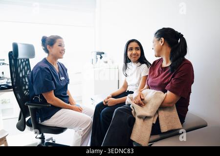 Smiling female doctor talking with mother and daughter sitting on examination table in medical clinic Stock Photo