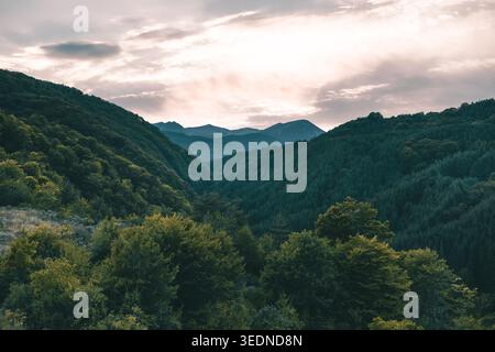 panoramic mountain landscape with green forested hills under dramatic cloudy sky at sunset Stock Photo
