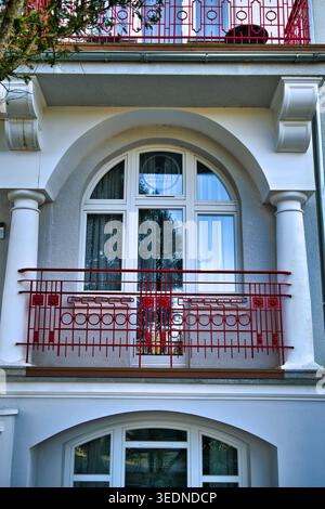 Elegant Arched Window And Red Balcony Railing On Classic White Building Facade With Columns - The seaside town of Świnoujście. Stock Photo
