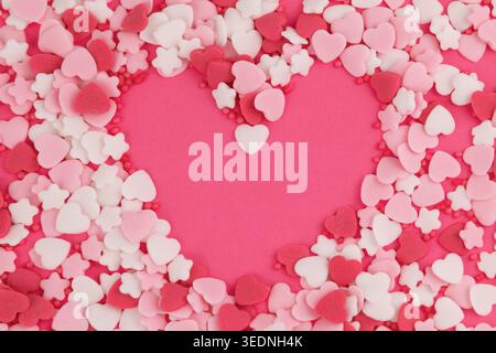 Heart shaped sprinkles forming heart outline on pink. Stock Photo