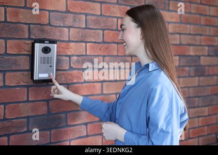 Woman pressing button on intercom panel near brick wall Stock Photo