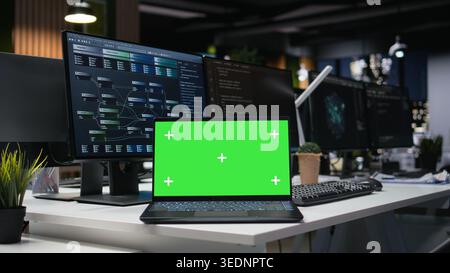Green screen laptop in modern high rise office late at night used for developing artificial intelligence algorithms. Mockup notebook in empty tech agency workplace building neural network Stock Photo