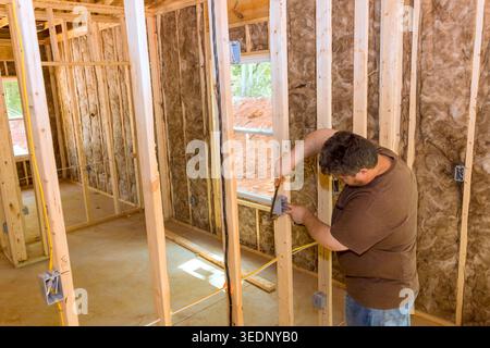 Worker uses measuring tool to mark wooden studs inside house progress in construction site. Stock Photo
