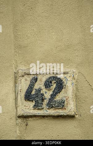 Weathered cast iron number 42 sign on aged wall with wide copy space and grunge urban texture. Stock Photo