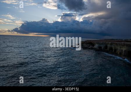 Dramatic clouds over rocky coastal cliffs at sunset Stock Photo