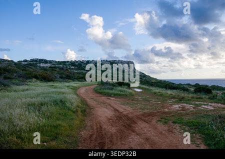 Dirt Road Curving Through Coastal Landscape Under Cloudy Sky Stock Photo