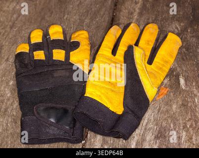 Pair of black and yellow leather gardening gloves, protective work wear, on wooden bench Stock Photo
