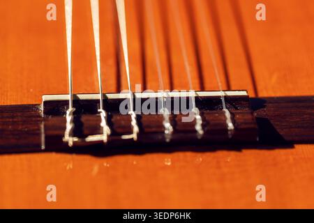 Bridge of classical guitar with nylon strings stretched across a warm orange soundboard. Detailed shot highlights the string anchoring mechanism and t Stock Photo