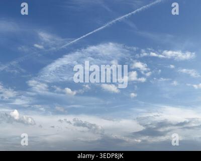 White high clouds in the center of the image Cirrocumulus and forming elongated Cirrus vertebratus, dissolving contrails from jet aircraft at the top Stock Photo
