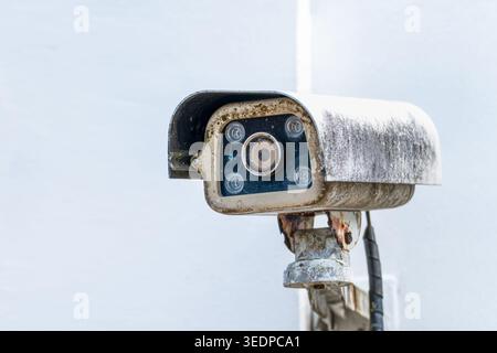 Old CCTV security camera mounted on wall and directed to monitor surroundings. Visible dirt, wear and corrosion emphasize long term usage and need for Stock Photo