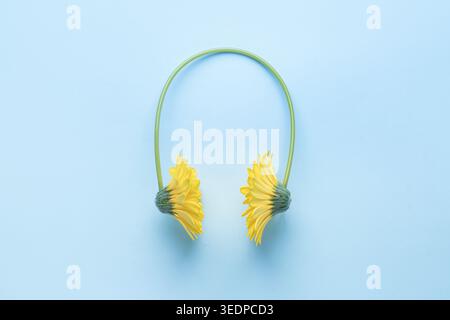 Minimal composition with yellow flowers shaped as headphones on blue background. Concept of music, audio, summer mood, relaxation and nature inspired Stock Photo