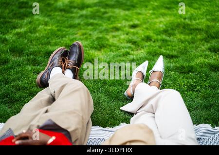 Fashionable african american couple lying on green lawn in park relaxing enjoying day outdoors. Stock Photo