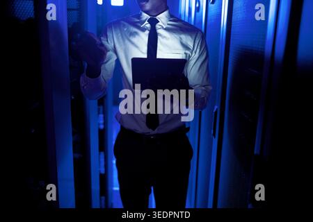 Hands, programmer and tablet in server room at night for research, coding and cybersecurity. Person, mainframe and overtime with digital for software Stock Photo