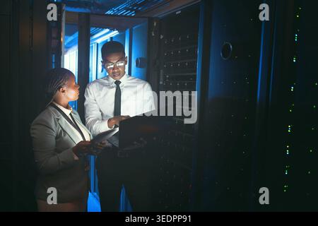 Inspection, review or engineers in server room with tech, teamwork or system check in data center. Technicians, laptop or black people in dark, fault Stock Photo