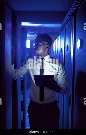 Black man, programming and tablet in server room at night for research, coding and cybersecurity. Person, programmer and overtime with tech software Stock Photo