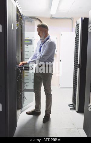Technician, cybersecurity and man on laptop in server room for diagnostics, inspection or network. Database, mature and person on computer for Stock Photo