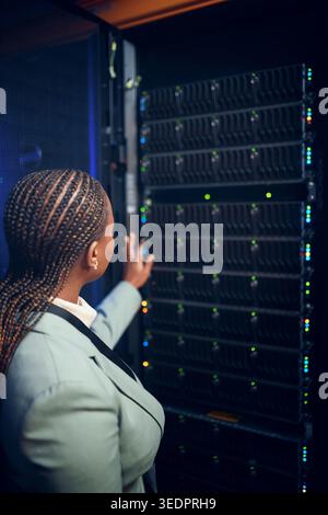 Back, black woman and programmer with mainframe at data center for inspection, cybersecurity and repairs. Person, developer and server room for Stock Photo
