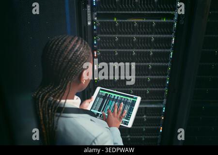 Woman, tablet and coding with maintenance in server room for cybersecurity, system or check for hardware. Programmer, tech and back on app ui for Stock Photo
