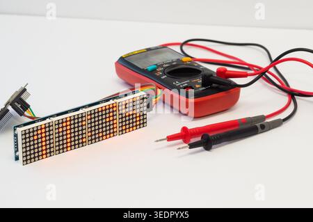 Multimeter with test probes and a Wi-Fi clock with seven-segment displays and ESP32 lie on a white background. Stock Photo