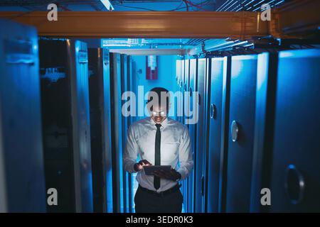 Server room, dark and black man on tablet for network system, diagnostics and cybersecurity. IT technician, hardware and person on tech for Stock Photo