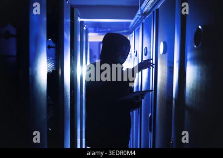 Criminal, person and hacking with tablet in server room for coding, cyberattack and data breach. Suspicious, hacker and digital with mainframe for Stock Photo
