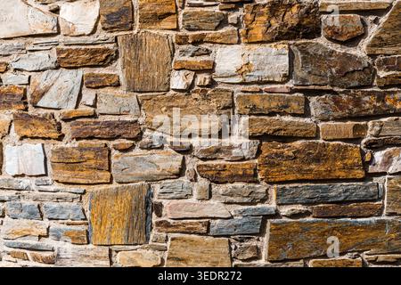 Rustic stone wall featuring various natural rock shapes and colors, creating a textured surface. Perfect as a background Stock Photo
