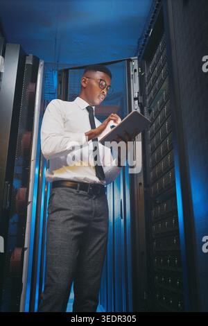 Black man, tablet and typing for inspection in server room with cybersecurity, system report and hardware. Programmer, tech and application for Stock Photo