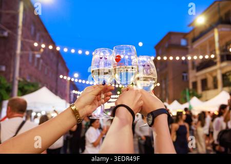 At Yerevan Wine Days Festival visitors raise three glasses of white wine in a toast on a city street on June 7, 2024, in Yerevan, Armenia. Stock Photo