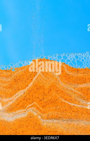 Orange sand falling onto peak against blue background, topped with delicate layer bubbles Stock Photo