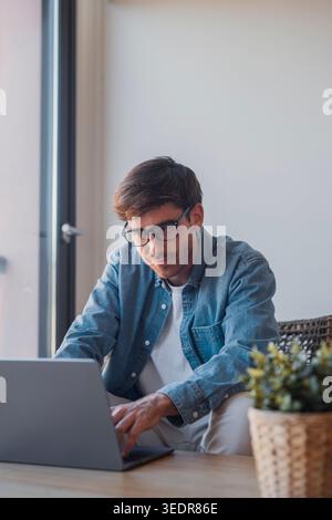 A young European businessman works at his desk using a laptop and technology apps for online learning and business tasks, showing focus and productivity in a modern office environment Stock Photo