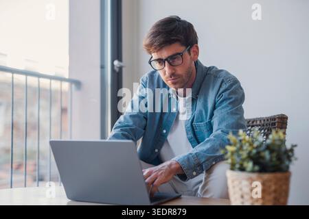 Young European businessman using laptop and technology apps for work or online learning, hispanic professional working at desk in office, focused on business tasks Stock Photo