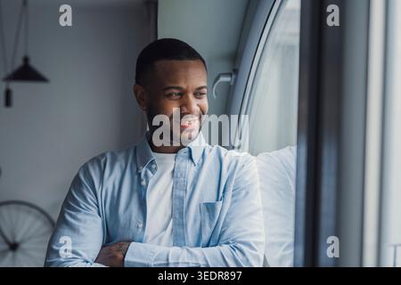 Smiling dreamy African American man thinking about future or new opportunities, positive pensive businessman at window looking to aside, planning, pondering strategy, business vision concept Stock Photo