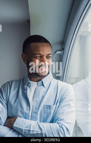 A dreamy Black professional gazes out the window with a calm smile, reflecting on business goals, new possibilities, and long-term vision in a modern workplace setting Stock Photo