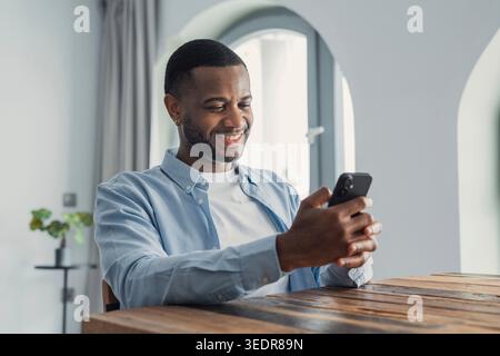 Smiling cheerful African American man looking at phone screen, reading good news in message, having fun with mobile device, browsing apps, playing funny game or chatting in social network Stock Photo