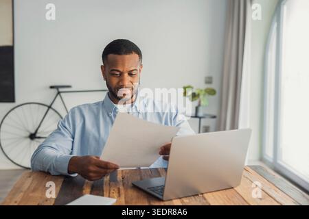 Concentrated African American manager reading letter, paper handout, analyzing company statistics, thinking about financial risks, comparing results. Thoughtful black worker considering business offer Stock Photo