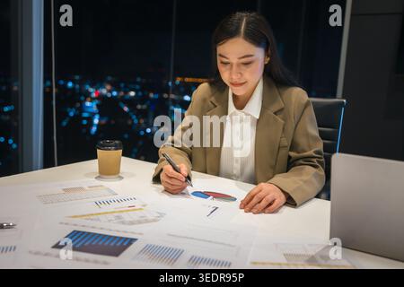 businesswoman thinking and analyzing business reports late at night in high-rise office with city lights background Stock Photo