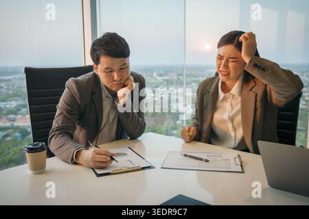 two business partners meeting and looking at documents with stressed and tired expressions in modern office Stock Photo