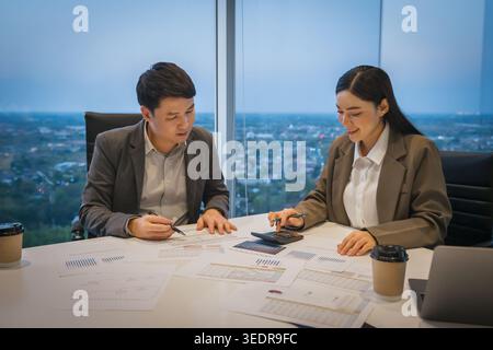 two business colleagues meeting and discussing financial reports and using calculator to data analysis in modern office at night Stock Photo