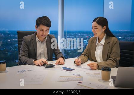 two business colleagues meeting and discussing financial reports and using calculator to data analysis in modern office at night Stock Photo