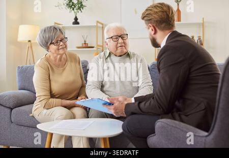 Senior couple sitting on sofa and talking to financial advisor about retirement insurance options. Stock Photo
