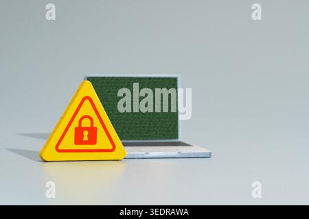 A warning sign with a red padlock icon and a laptop displaying green binary code. Cyber security, data encryption, ransomware concept. Stock Photo