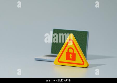 A warning sign with a red padlock icon and a laptop displaying green binary code. Cyber security, data encryption, ransomware concept. Stock Photo