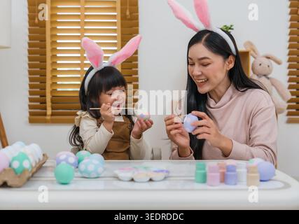 mother and preschool child girl wearing bunny ears painting and decorating egg  together at their home on easter day. happy family holiday activity co Stock Photo