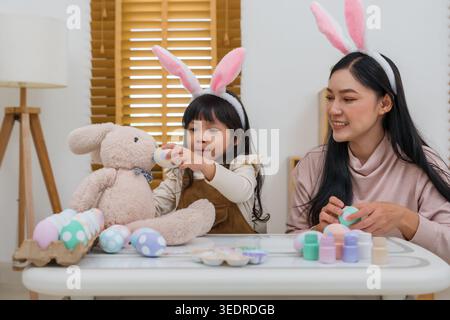 happy preschool child girl and mother celebrating Easter day with stuffed rabbit and colorful eggs on table at their home Stock Photo